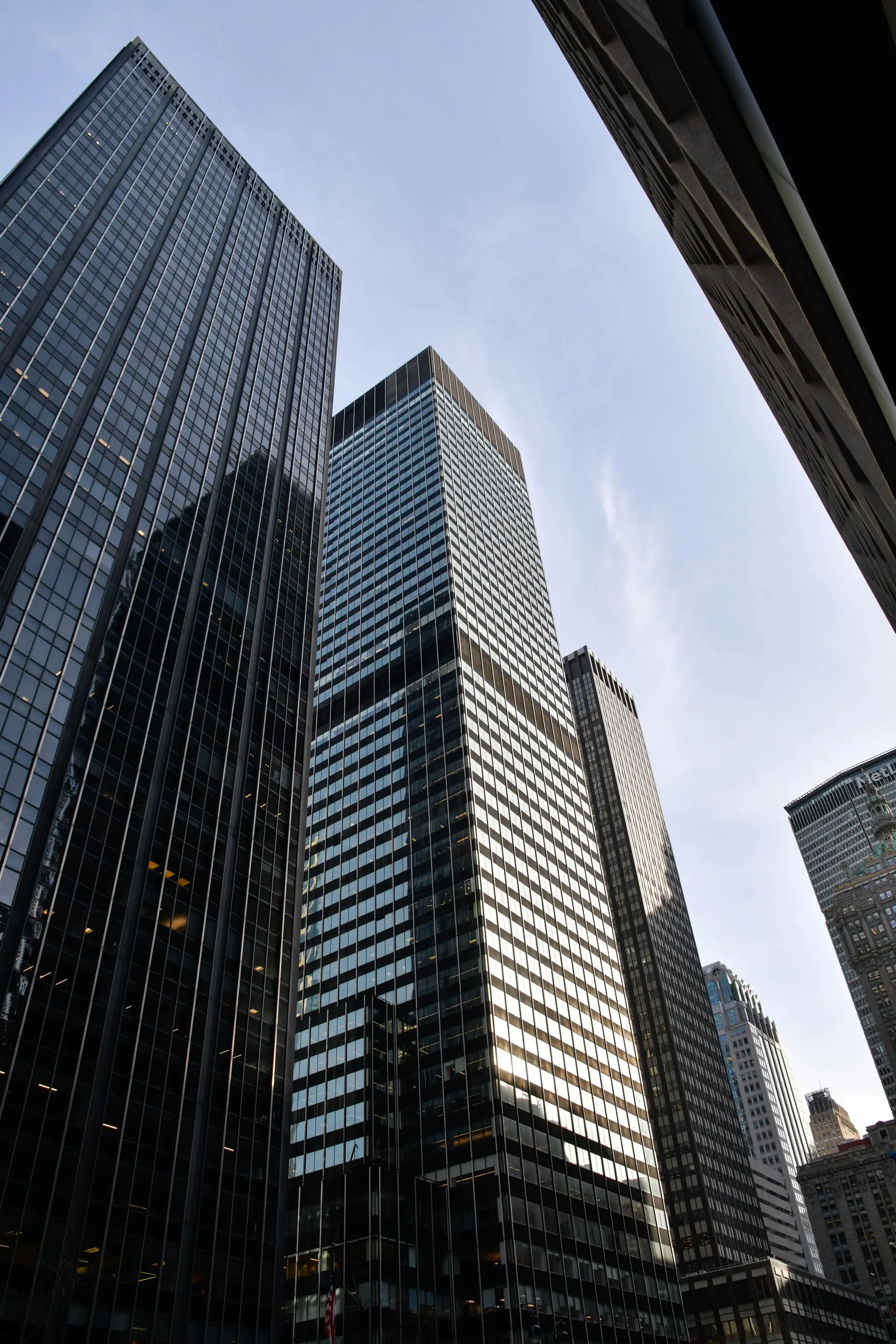 Blick von unten auf die Glasfassaden mehrerer Hochhaustürme eines Finanzviertels.