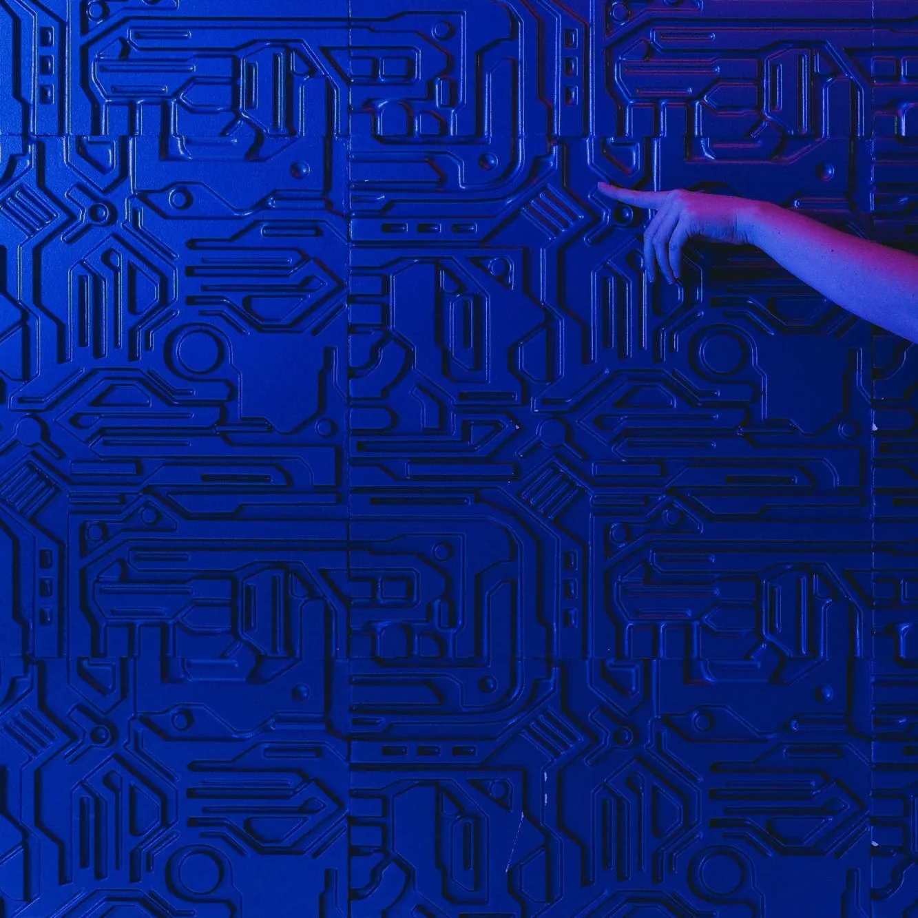 Eine Hand zeigt auf eine blau beleuchtete Wand aus Leiterbahnen.
